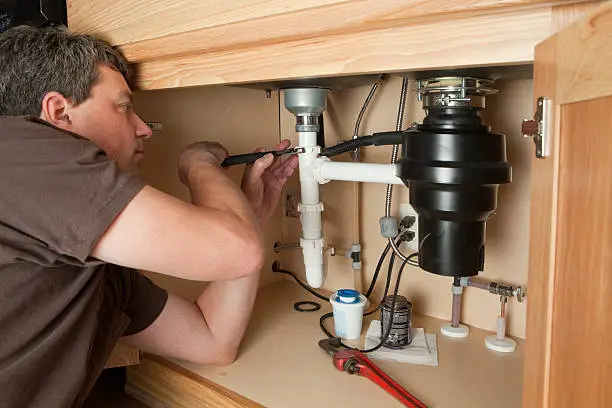 Plumber fixing garbage disposal under kitchen sink – professional garbage disposal repair in Norman OK